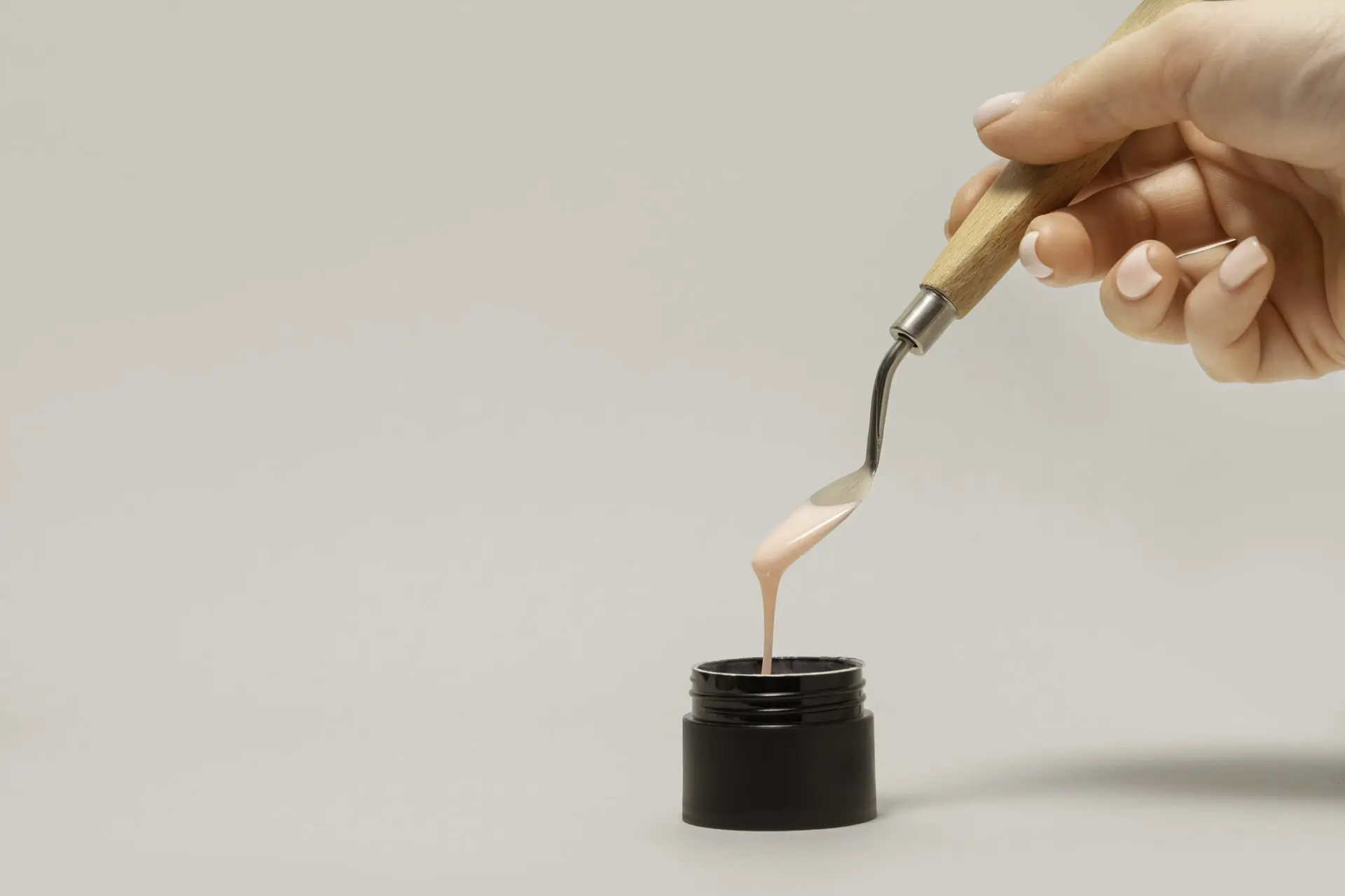 Na zdjęciu widać lakier oraz dłoń wyciągająca go ze słoiczka