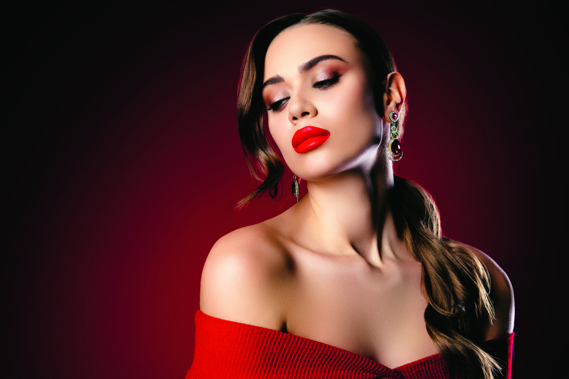 Glamorous young female model with striking makeup and accessories against a rich red backdrop, exuding elegance and sophistication.