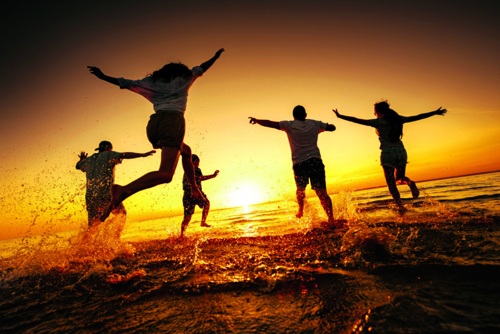 Silhouettes of big group of happy young friends are having fun, run and jump at calm sunset lake beach