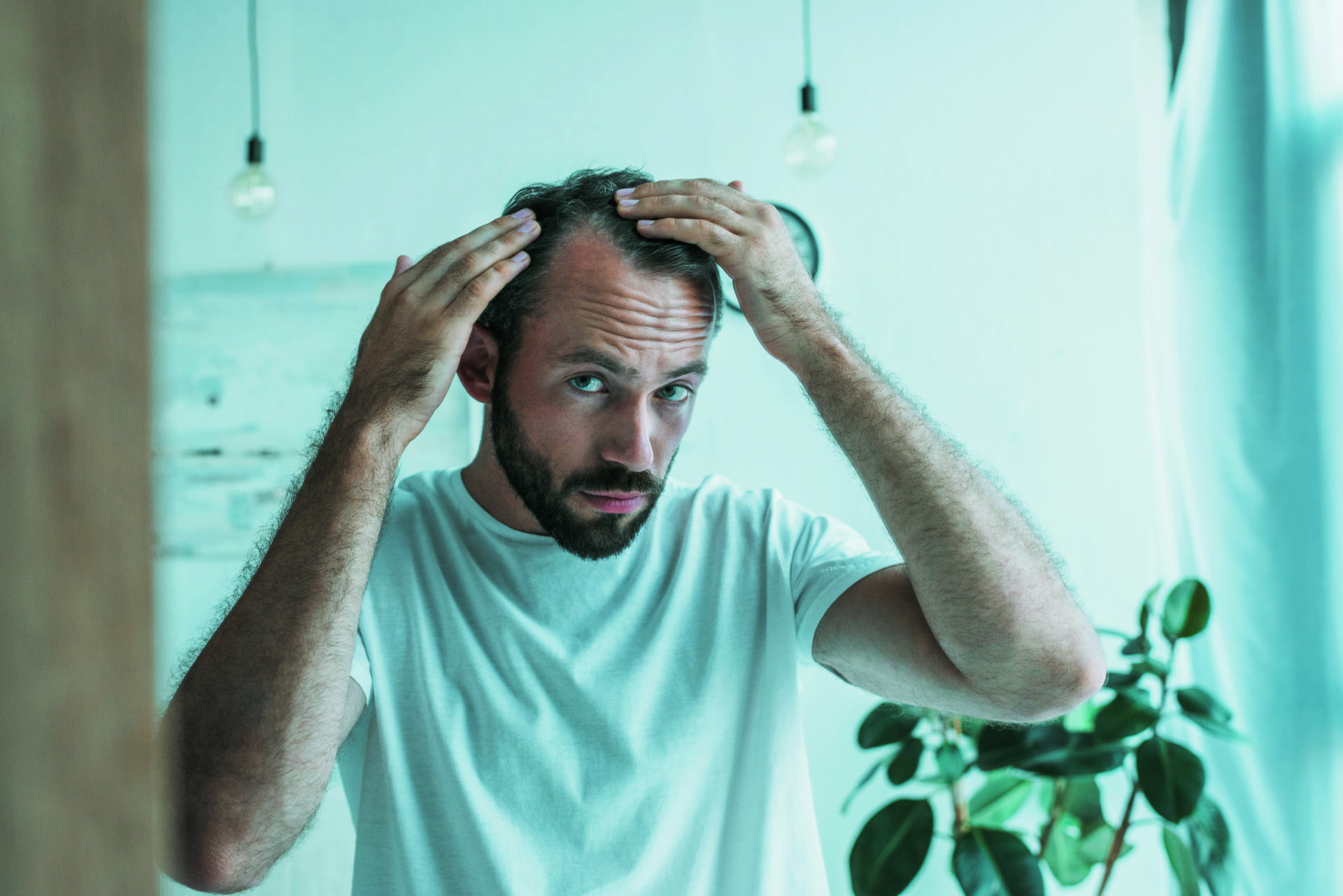 mężczyzna w średnim wieku z łysiną, patrzący w lustro; motyw wypadania włosów