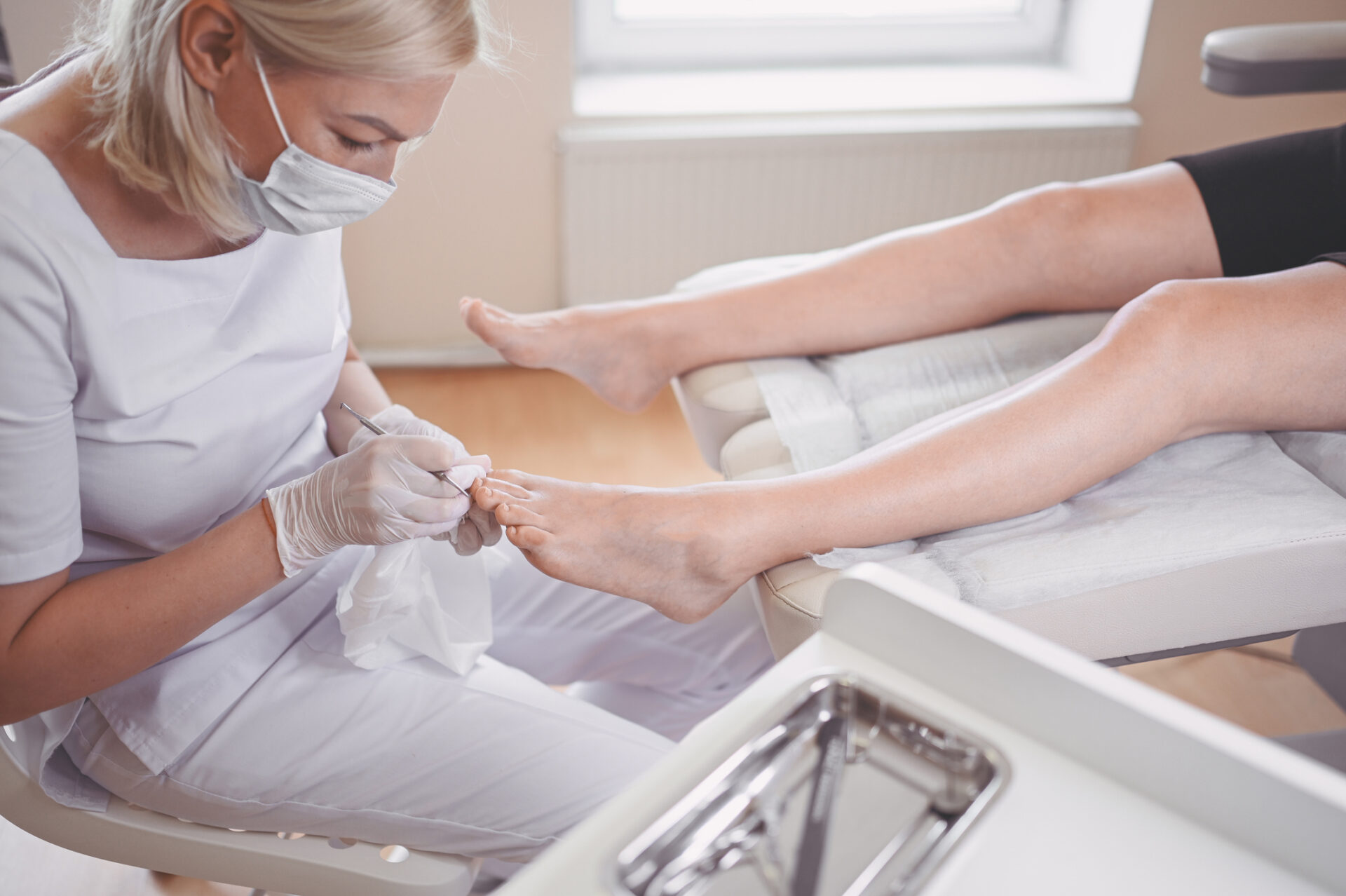 Zbliżenie na profesjonalny zabieg pedicure przy użyciu podwójnego narzędzia do paznokci. Pacjentka podczas wizyty u podologa. Zabieg na stopy w salonie SPA. Klinika podologiczna. Ręce pedicurzystki w białych rękawiczkach
