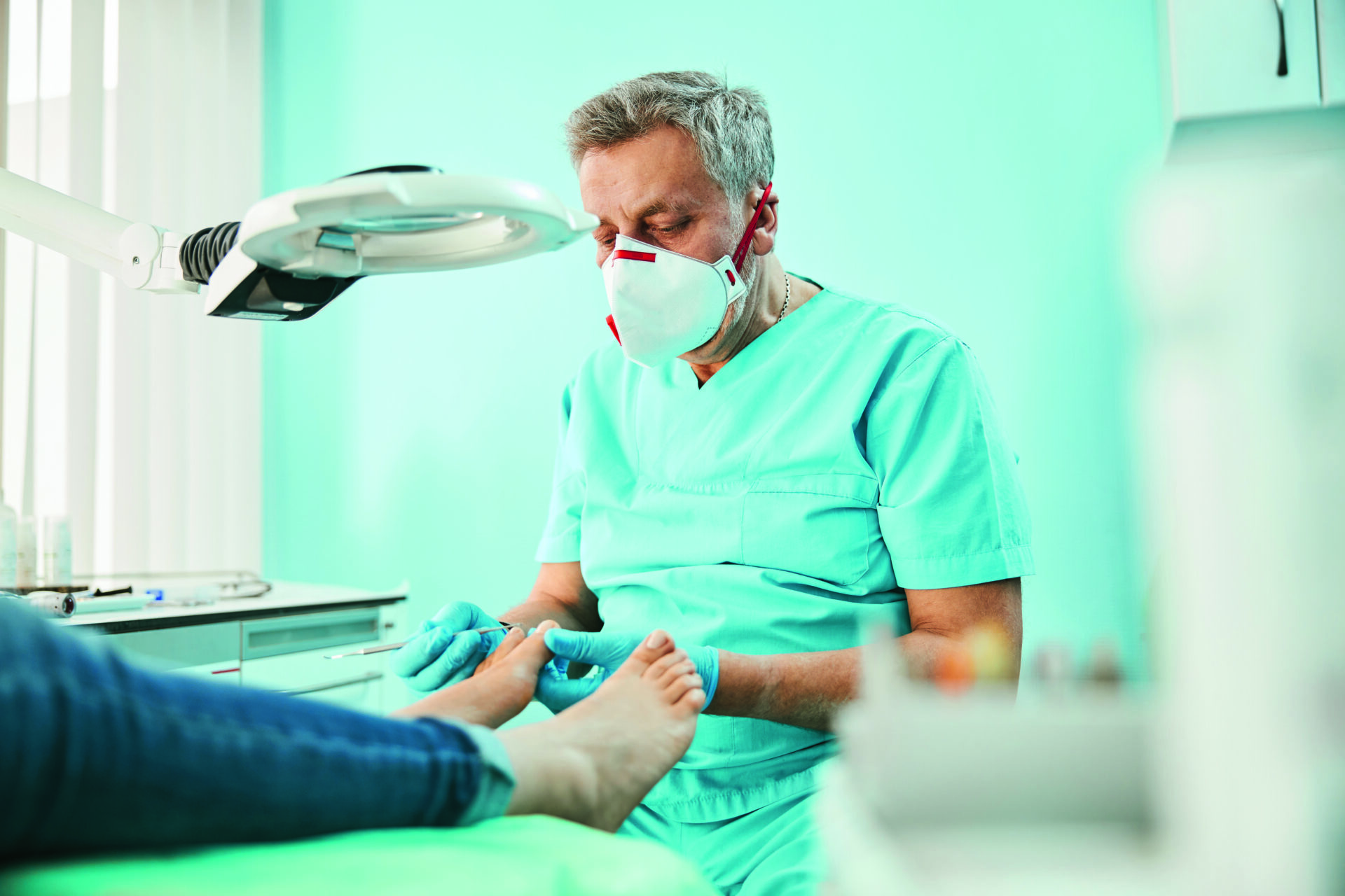 Portret od pasa w górę przedstawiający pewnego siebie, przystojnego mężczyznę w maseczce medycznej, wykonującego zabieg pedicure medycznego w gabinecie kosmetycznym