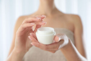 Young woman holding jar of cream at home, closeup