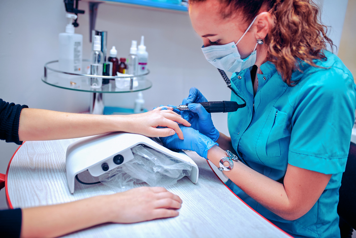 Manicurist removing cuticle from the girl client nail at beauty salon.