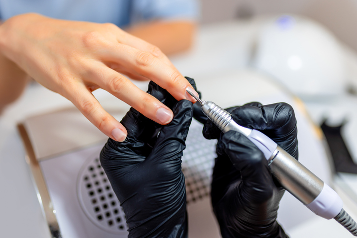 Profesjonalna manikiurzystka korzystająca z urządzenia elektrycznego w salonie kosmetycznym. Kobieta w salonie kosmetycznym podczas wykonywania manicure.