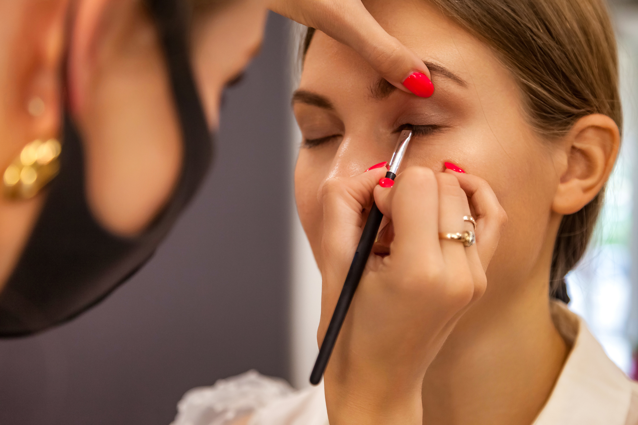 Podczas wizyty w salonie klientka korzysta z profesjonalnego makijażu oczu. Wizażystka nakłada eyeliner na powiekę klientki w studiu.